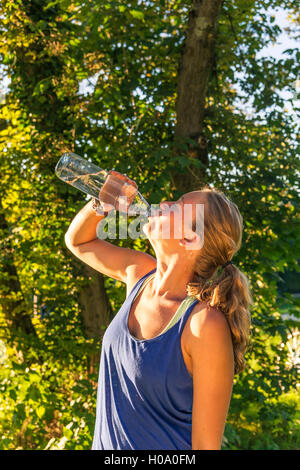 Giovane donna in abbigliamento sportivo di acqua potabile da una bottiglia, Baviera, Germania Foto Stock