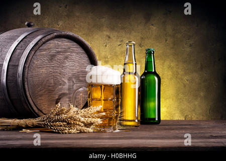 Boccale di birra con il giallo e il verde bottiglia su uno sfondo di botti di legno Foto Stock