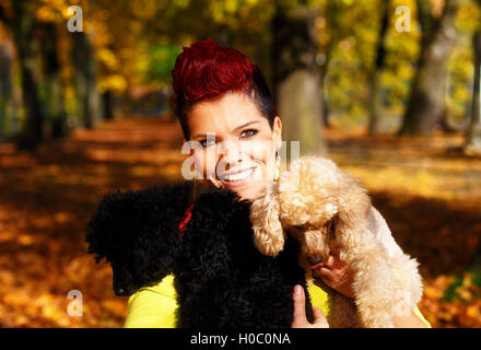 Carina ragazza sorridente con il bianco e nero cane e abbracciando in autunno parcheggiare all'esterno. Contatto con gli occhi. Foto Stock