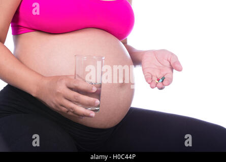 Close-up della donna incinta mano con un bicchiere di acqua e pillola isolato su sfondo whie Foto Stock