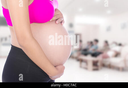 Close-up della donna incinta ventre con la sua mano su di esso in background in ospedale Foto Stock