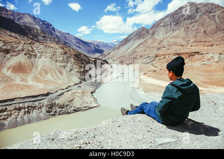 Giovane uomo felice seduto sulla scogliera sul viaggio nel fiume Indo in Leh, Ladakh, India Foto Stock