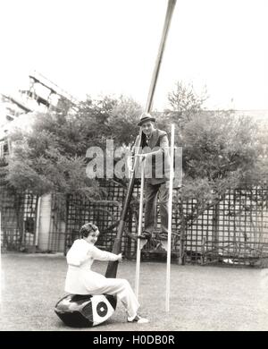 L'uomo su palafitte di tenere su giant golf club con donna seduta su di esso Foto Stock