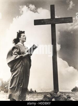 Donna cantare inni di una grande croce di legno su una collina Foto Stock