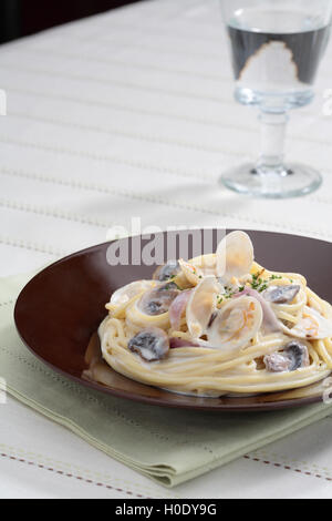 Bonggolre salsa di panna e la pasta con le vongole sulla piastra nera con un bicchiere di acqua Foto Stock