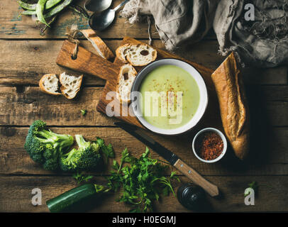 In casa il segnale di PEA, broccoli, zucchine minestra in crema in bianco ciotola con baguette fresca sulla tavola di legno su sfondo rustico, vista dall'alto, Foto Stock