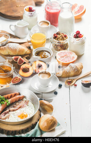 Uovo fritto con salsicce e bacon, pane, cornetti caldi con burro e marmellata, frutta, smoothie, succo d'arancia, yogurt, muesli con m Foto Stock