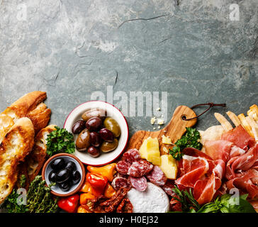 Il cibo italiano ingredienti sfondo con prosciutto, salame, parmigiano, olive, pane bastoni su pietra ardesia Foto Stock