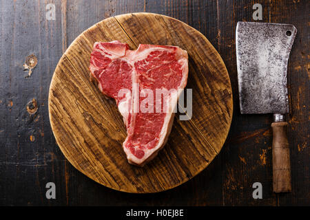 Materie carni fresche T-bone steak e Butcher cleaver sul taglio di chopping board su sfondo di legno Foto Stock