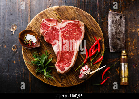 Materie carni fresche T-bone steak, stagionatura e Butcher cleaver sul taglio di chopping board su sfondo di legno Foto Stock