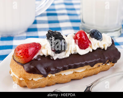 Eclair al cioccolato con frutti di bosco e panna montata sulla parte superiore. Foto Stock