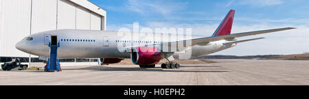 Grande aereo passeggeri di colore rosso e bianco parcheggiata vicino hangar Foto Stock