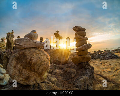 Piramide di pietre sulla sabbia che simboleggiano zen, armonia, equilibrio. Oceano al tramonto in Khao Lak Thailandia Foto Stock