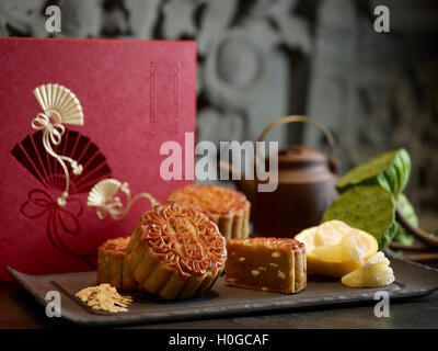 Mooncake orientali con argento lotus incolla yuzu e semi di melone sul piatto nero con tè pentola Foto Stock