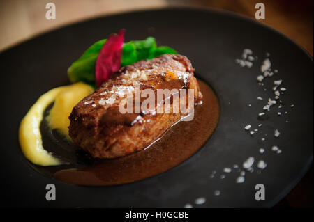 Arrosto di filetto di manzo con salsa di pomodoro e lattuga sul piatto nero Foto Stock