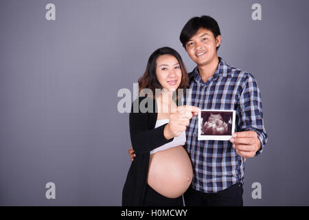 Felice di gravidanza e il marito che mostra immagine ad ultrasuoni su muro grigio sfondo Foto Stock