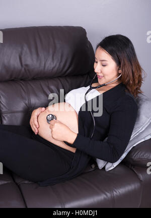 Donna incinta l'ascolto del bambino con heartbeat stetoscopio posto sul suo ventre Foto Stock
