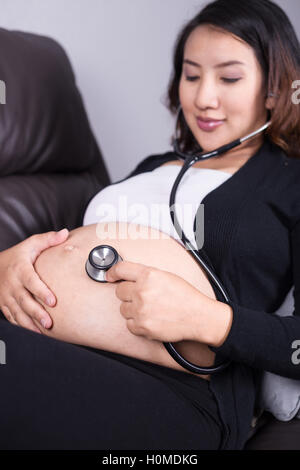 Donna incinta l'ascolto del bambino con heartbeat stetoscopio posto sul suo ventre Foto Stock