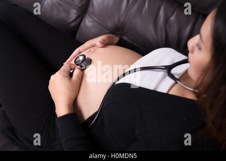 Donna incinta l'ascolto del bambino con heartbeat stetoscopio posto sul suo ventre Foto Stock