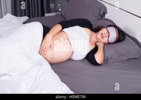 Donna incinta di dormire sul letto nella camera a casa Foto Stock