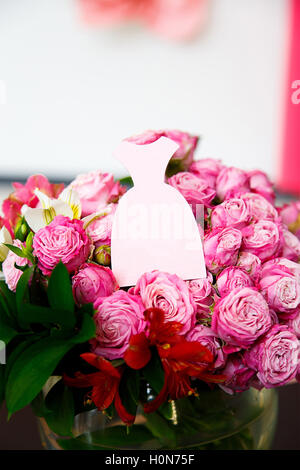 Una carta in forma di abito rosa su bouquet di rose rosa Foto Stock