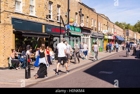 La gente che camminava davanti a negozi locali e ristoranti in Broadway Market, East London, in una giornata di sole. Foto Stock