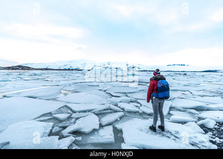Donna in piedi sul ghiaccio floe, Jökulsárlón laguna glaciale, bordo meridionale del Vatnajökull, Regione meridionale Islanda Foto Stock