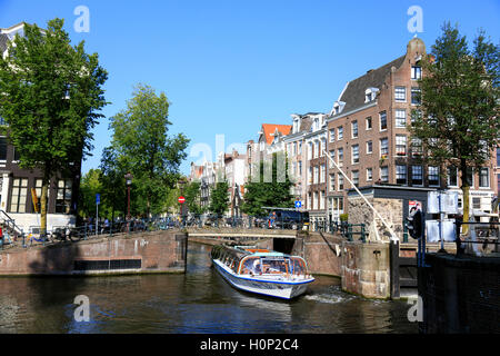 Imbarcazione turistica passa sotto uno dei ponti sui canali di Amsterdam Foto Stock