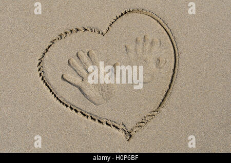 Handprints e cuore disegnato sulla sabbia bagnata Foto Stock