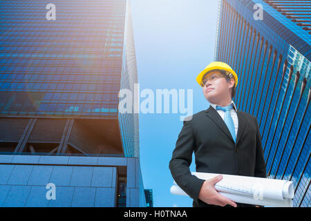 Giovane ingegnere di progettazione con elmetto blueprint di tenuta in mano per la gestione del business plan. Foto Stock