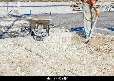 Lavoratore è ghiaia di livellamento con la pala al nuovo posto di parcheggio mediante la rimozione del materiale in eccesso. Foto Stock