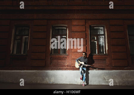 L'uomo gioca il gitar sullo sfondo della parete Foto Stock