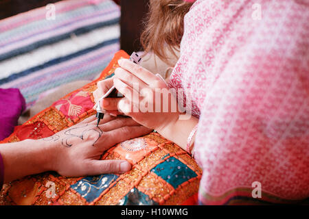 Giovane donna artista mehendi pittura henna sulla mano per uomo Foto Stock
