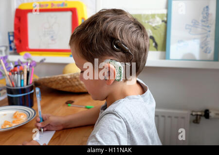 Giovane studente sordo di ragazzo con impianti cocleari di 6 anni disegno scrivere su carta con la penna seduta a casa In Gran Bretagna KATHY DEWITT Foto Stock