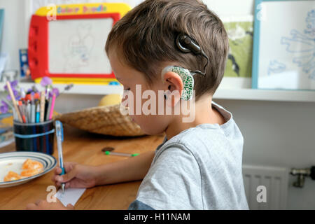 Bambino sordo con impianto cocleare di 6 anni che disegna con carta da penna seduto al tavolo di casa in Gran Bretagna, Regno Unito, KATHY DEWITT Foto Stock