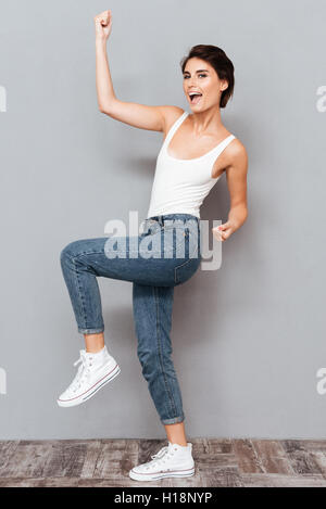 A piena lunghezza Ritratto di una giovane donna che celebra il suo successo isolata su uno sfondo grigio Foto Stock