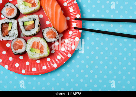 Alta angolazione alcuni dei differenti makizushi e nigirizushi in una targhetta rossa modellato con punti bianchi e un paio di bacchette o Foto Stock