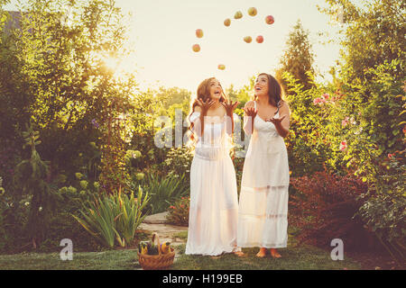 Due graziosi sorelle in lunghi vestiti bianchi si lancia fino al raccolto di mele e di pere. Frutti maturi e verdure. un abbondante raccolto Foto Stock