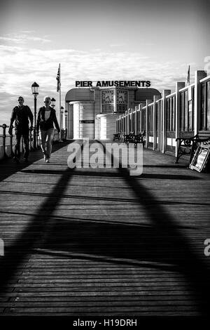 Un giovane a piedi come "leader Linee' ombre di un corrimano crea un percorso sul decking di Worthing Pier Foto Stock