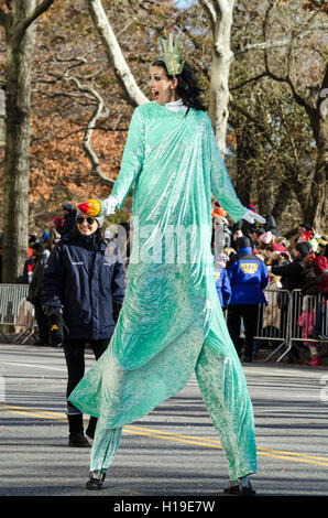 Un stiltwalker vestita come la Statua della Libertà sorride alla folla guardando il Macy's Thanksgiving Day parade. Foto Stock