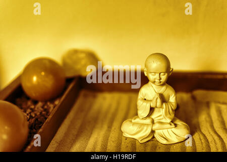 Statua del Buddha nella posizione del loto seduto sulla sabbia. Concetto di Ayurveda. Il Buddha in giardino Zen con linee lisce in sabbia. Foto Stock