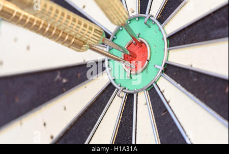Tre freccette in metallo hanno colpito il red bullseye su un dart board Foto Stock