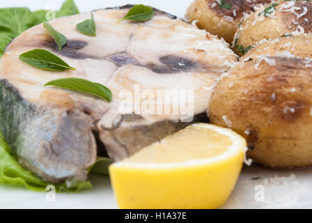 Rosso fritto bistecca di tonno servita con un pezzo di limone e patate cotte sulla piastra bianca closeup. Foto Stock