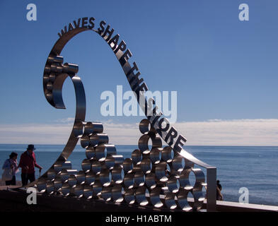 A mezzogiorno sull'equinozio autunnale la gente gode del sole glorioso sul lungomare presso la scultura delle onde, Seaton, in Devon. Foto Stock