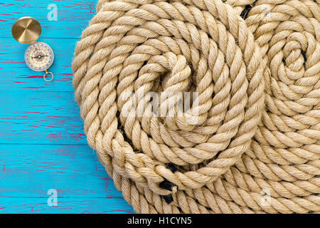 Due avvolto ordinatamente le funi e una bussola magnetica su un colorato crepitare la vernice sfondo blu in un concetto di marine rigging, boa Foto Stock