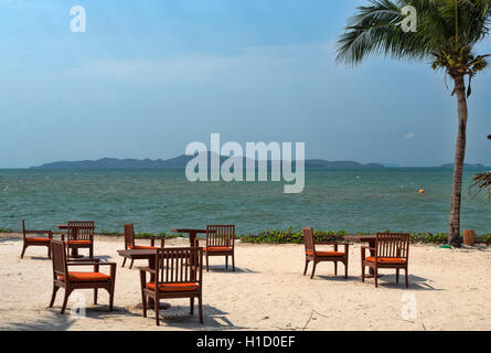 Tavole di ristorante sulla spiaggia con un albero di palme che si affaccia sul mare. Foto Stock