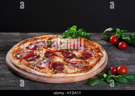 Freschi e deliziosi salsiccia per pizza pizza con salumi , bacon , pepe rosso, verde cipolle e formaggio sullo sfondo di legno. Vista dall'alto. Foto Stock