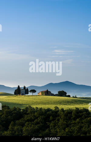 Verde tipico paesaggio toscano in Val d'Orcia con la fattoria e la cappella sulla collina, campi, cipressi, alberi e il blu cielo molto nuvoloso Foto Stock