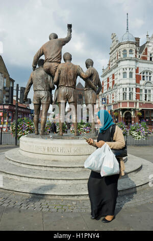Donna musulmana passeggiate passato la Coppa del Mondo di scultura denominata anche la Champions, vicino vicino al West Ham United Football Club del vecchio Upton Park Stadium, dotate di Bobby Moore, Geoff Hurst, Martin Peters e Ray Wilson, eroi del 1966, Inghilterra la vittoria a Wembley. London.UK Foto Stock
