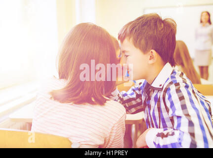 Sorridente schoolgirl whispering a classmate orecchio Foto Stock